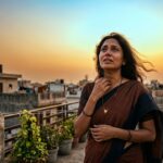 एक विचारमग्न महिला, आसमान की ओर देखती हुई, उसके चेहरे पर पीड़ा और आत्मविश्वास का मिश्रित भाव, प्रतीकात्मक रूप से नारी संघर्ष और आशा को दर्शाती हुई