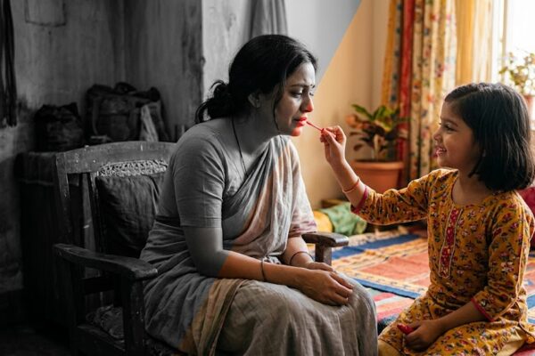 माँ और बेटी का भावुक दृश्य, बेटी अपनी माँ को लाल लिपस्टिक लगाते हुए, जीवन में रंग लौटने का प्रतीक
