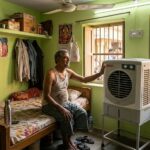 भीषण गर्मी में कमरे में चलता कूलर और राहत महसूस करता व्यक्ति, मानवीय संवेदना और पड़ोसी सहयोग का दृश्य।