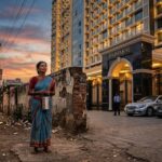 A poor woman in a faded saree stands near a luxurious modern apartment building