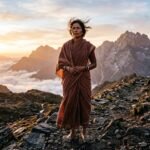सूर्योदय के समय चट्टान पर आत्मविश्वास से खड़ी भारतीय महिला, चेहरे पर दृढ़ता और शक्ति का भाव।