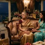 भव्य बंगले में जन्मदिन समारोह के बाद अकेली बैठी एक महिला, जिसके पास उसकी बहू सहानुभूति से बैठी है, रिश्तों और मानवता का भावनात्मक दृश्य।