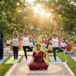 A diverse group of Indian people, including children, adults, and senior citizens, practicing yoga together in a green park at sunrise, promoting health, wellness, and community spirit.