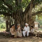 विशाल बरगद के पेड़ की छाँव में बैठे बुजुर्ग और परिवार